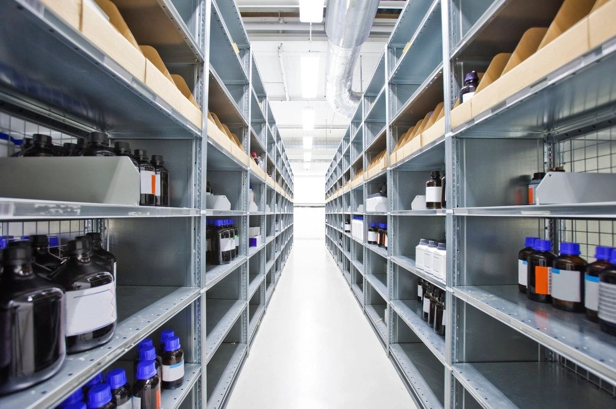 Empty industrial metal shelves in a warehouse aisle with bright overhead lighting.