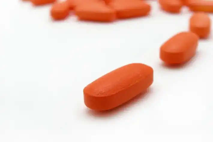 Close-up of an orange oblong pill on a white surface.