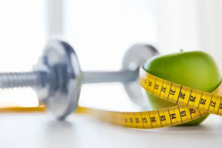 A dumbbell and measuring tape on a white surface symbolizing fitness.