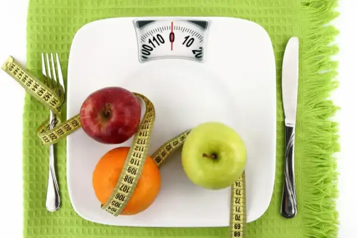 A scale with fruits, a measuring tape, and cutlery symbolizing healthy eating.