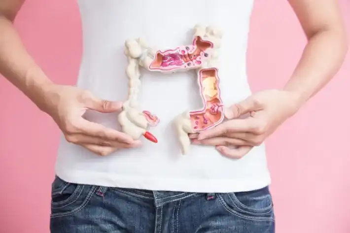 Person holding a pink tampon near their abdomen against a pink background.