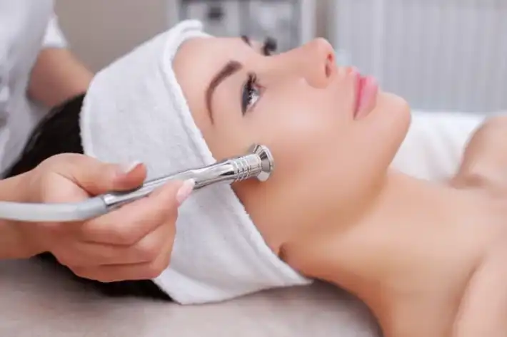 Woman receiving a facial treatment with a handheld device.