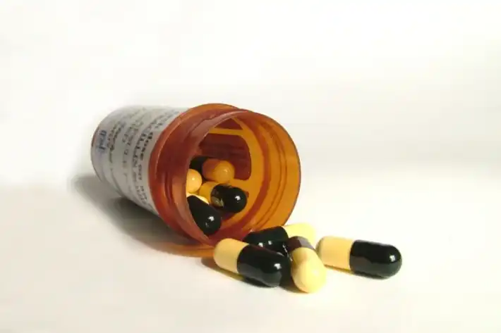 Capsules spilling out of a prescription bottle on a white surface.