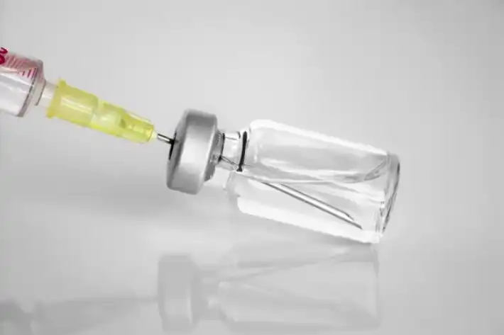 A syringe drawing liquid from a small medicine vial.