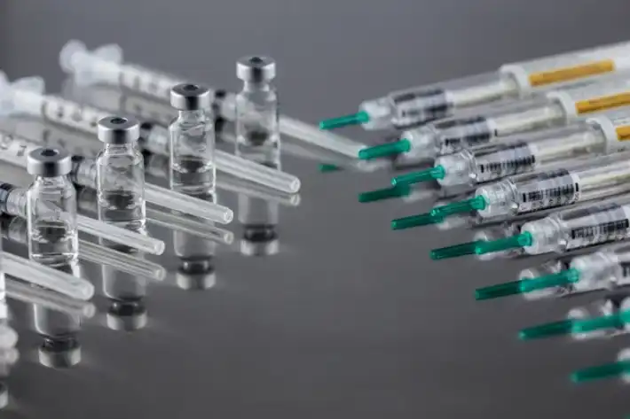 Medical syringes and vials arranged on a reflective surface.