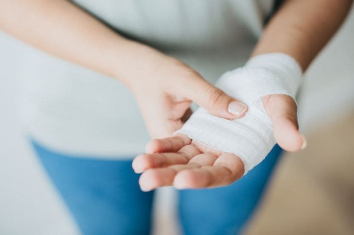 Person with a bandaged hand holding a cotton pad.