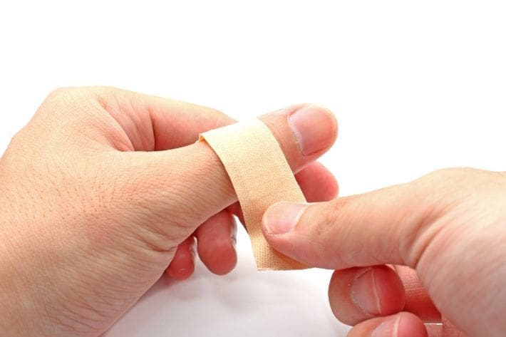 Person applying a beige adhesive bandage to their thumb.