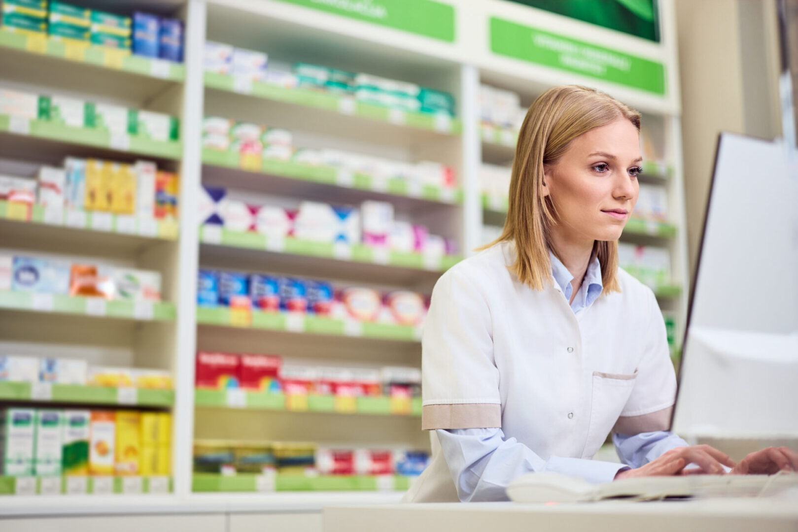 Professional pharmacist using computer while working in a modern, well-stocked pharmacy